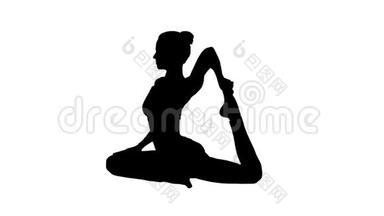 剪影美丽的年轻女子做瑜伽或普拉提运动。 一个鸽子国王的姿势，EkaPada Rajakapotasana。